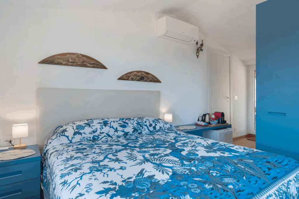 Camera Blu bedroom with blue and white floral bedding, white headboard, and blue accents. Hotel room interior.