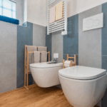 Camera Blu bathroom. Toilet and bidet with blue and gray striped wall. Towel rack and wooden floor.