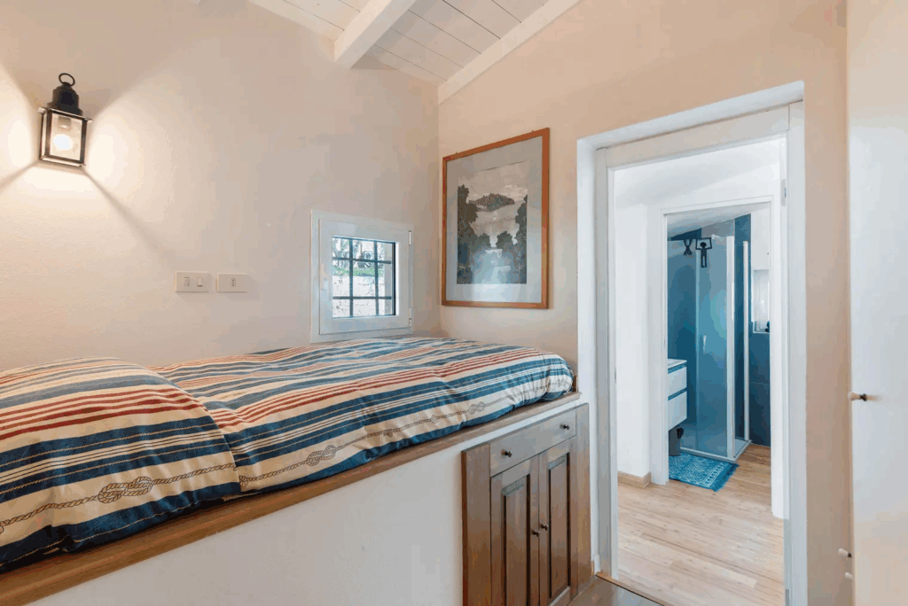 Camera Blu room: Interior view of bed with nautical striped bedding, small window, and bathroom with blue shower.