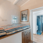 Camera Blu room: Interior view of bed with nautical striped bedding, small window, and bathroom with blue shower.