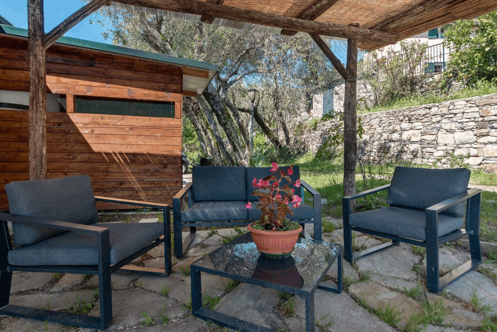 Camera Blu outdoor seating area. Patio furniture: chairs, sofa, table, and potted flowers under a rustic pergola.