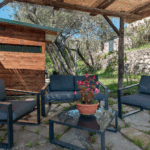 Camera Blu outdoor seating area. Patio furniture: chairs, sofa, table, and potted flowers under a rustic pergola.