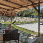 Camera Blu outdoor patio with seating, stone wall, and thatched roof. Relaxing garden view.