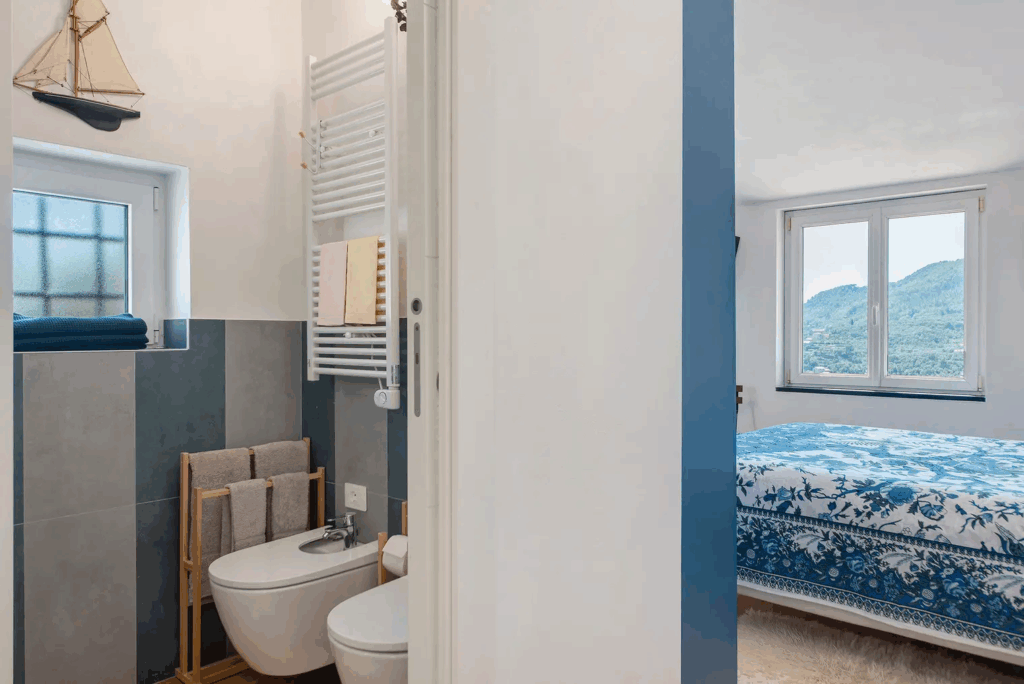 Camera Blu bathroom. Modern bathroom with bidet, towel rack, and blue accents. Bedroom view with mountain scenery.