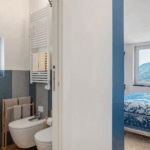 Camera Blu bathroom. Modern bathroom with bidet, towel rack, and blue accents. Bedroom view with mountain scenery.