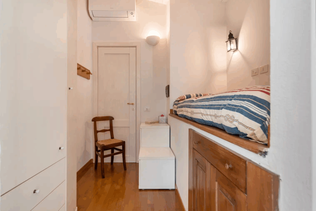 Camera Blu interior with bed nook, chair, and storage. Cozy room design.