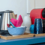 Camera Blu breakfast setup. Kettle, coffee machine, bowl with cutlery and napkins on a wooden tray.