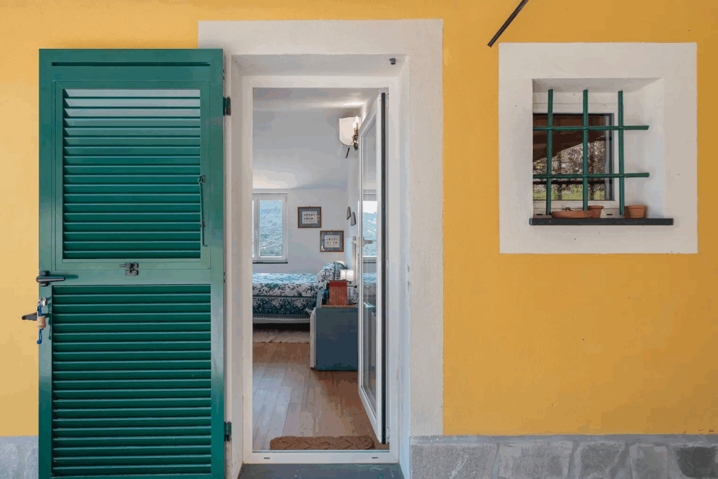 Camera Blu door. Exterior view of a yellow building with a green shuttered door and window. Interior view of bedroom.