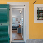 Camera Blu door. Exterior view of a yellow building with a green shuttered door and window. Interior view of bedroom.