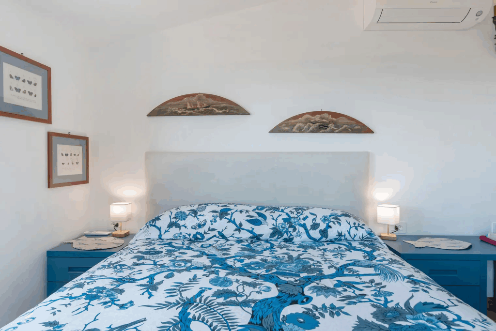 Camera Blu double bed. Bedroom with blue floral bedding, white walls, and blue nightstands.