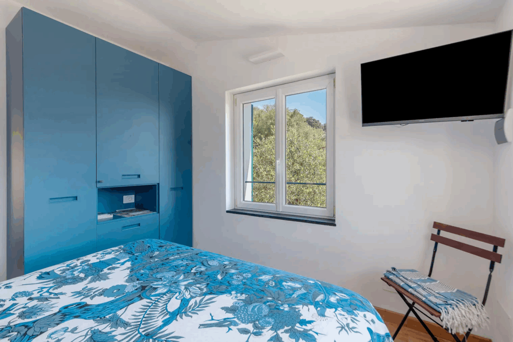 Camera Blu bedroom. Blue wardrobe, floral bedspread, window, and TV. Modern interior design.