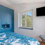 Camera Blu bedroom. Blue wardrobe, floral bedspread, window, and TV. Modern interior design.