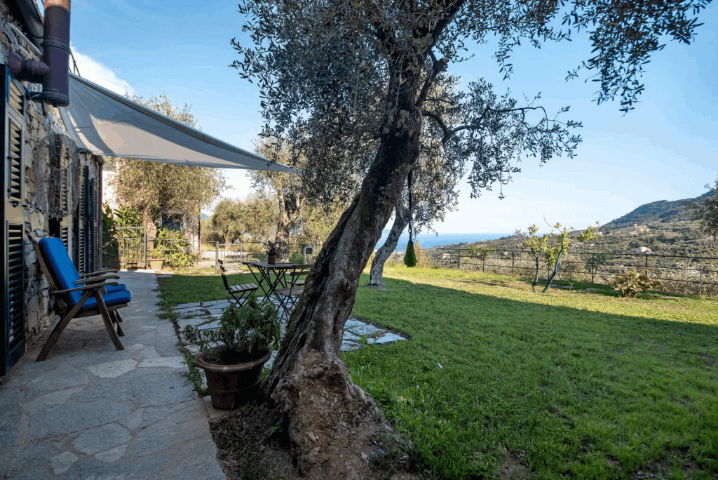 Casa di Pietra garden view. Stone house patio with chairs, table, and olive trees overlooking the landscape.