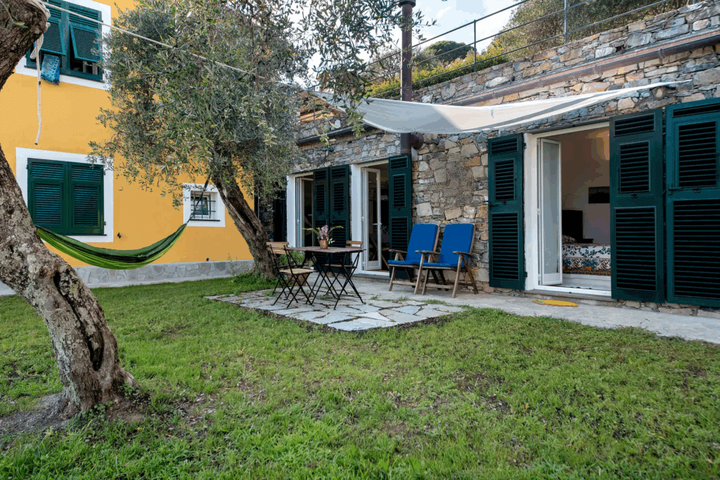 Casa di Pietra garden view. Stone house with outdoor seating, hammock, and green shutters.