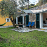 Casa di Pietra garden view. Stone house with outdoor seating, hammock, and green shutters.
