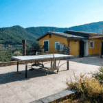 Casa di Pietra terrace view. Ping pong table on patio with mountain backdrop. Yellow building with blue shutters.